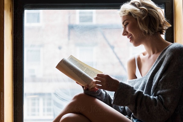 Woman reading book next to window